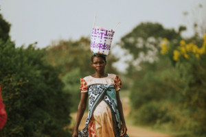 A pregnant African woman carrying a basket on her head while walking along a rural dirt road