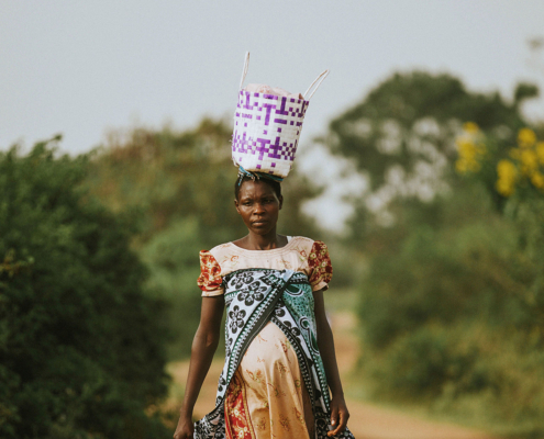 A pregnant African woman carrying a basket on her head while walking along a rural dirt road