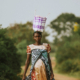 A pregnant African woman carrying a basket on her head while walking along a rural dirt road